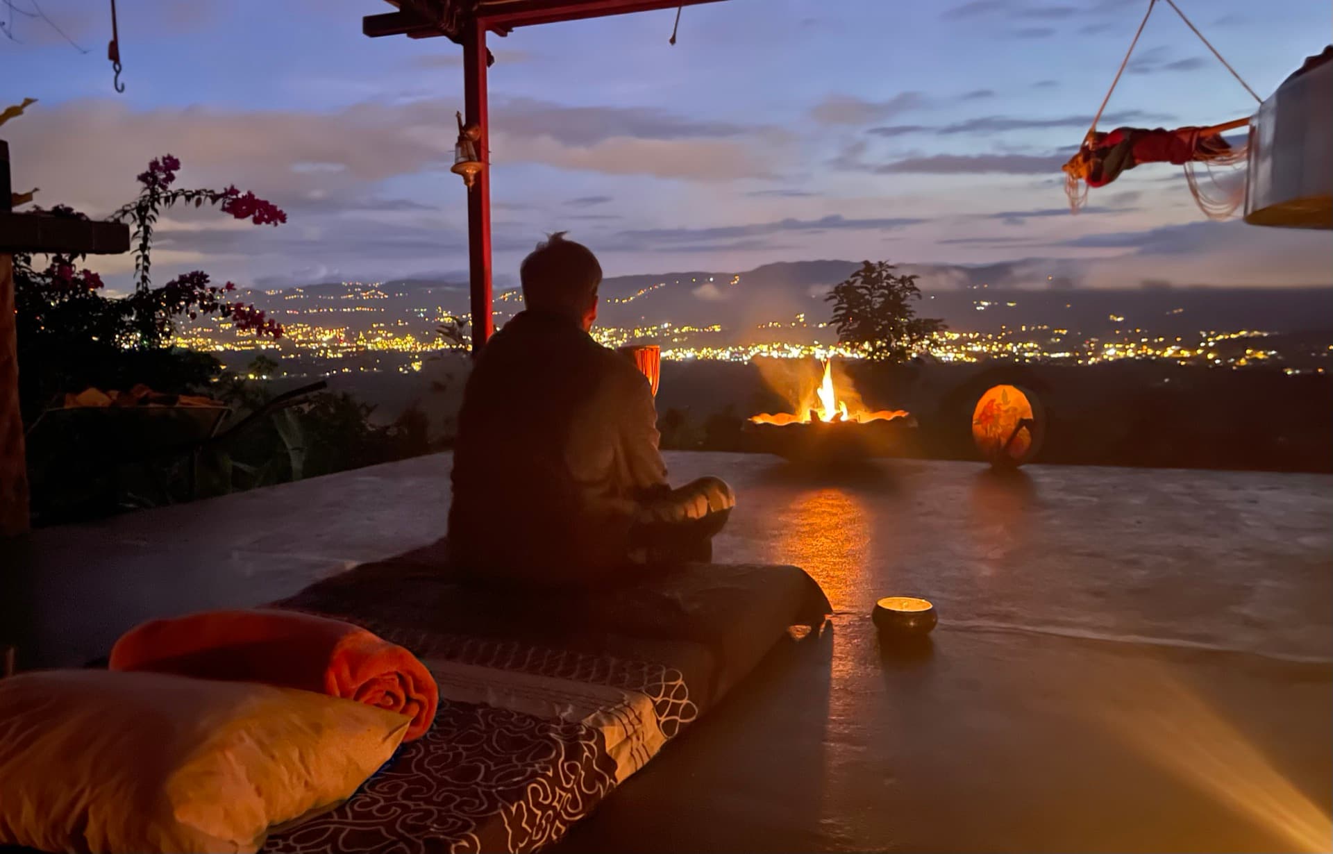 Meditation by fire with city lights at dusk